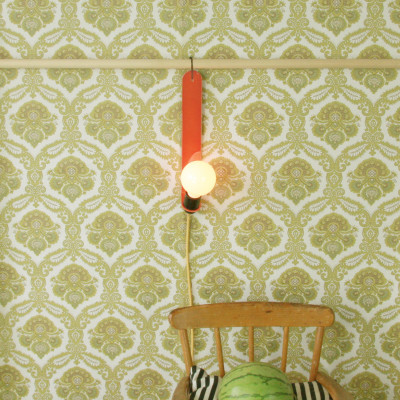 Lámpara de pared Skipper en color coral transparente delante de un papel pintado estampado.